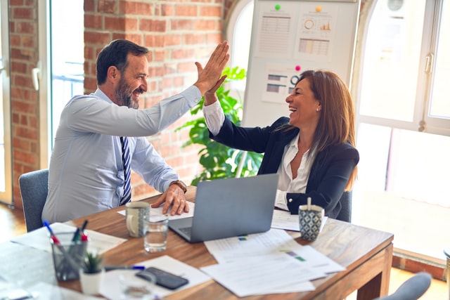 Two co-workers smiling at each other while exchanging a high five at the office